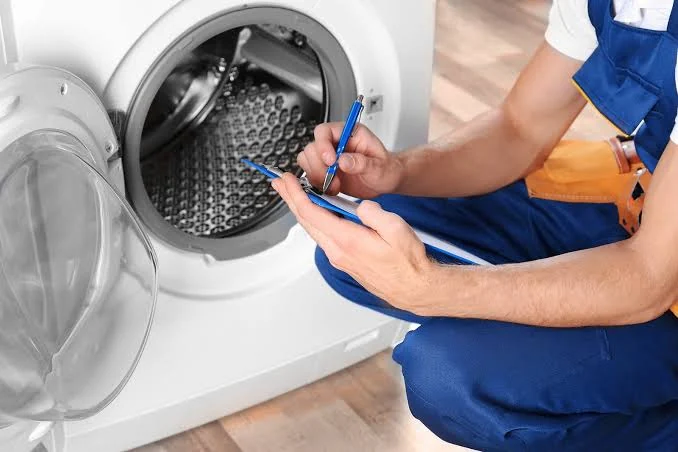 Appliance specialist recording diagnostic notes beside an open washing machine