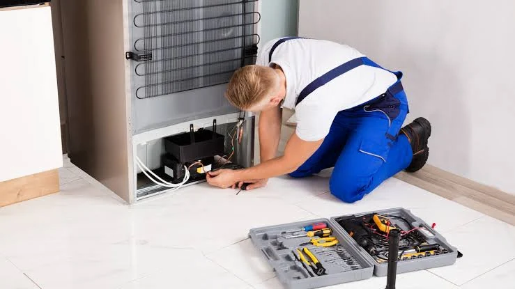 Technician checking the compressor area behind a refrigerator